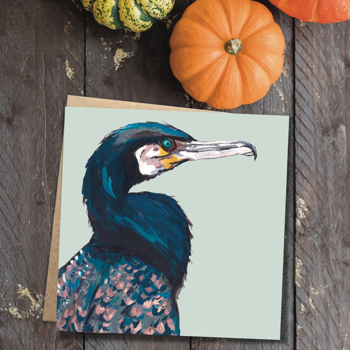 Cormorant bird illustration on a square greeting card displayed next to a rustic 100% recycled brown kraft paper envelope.