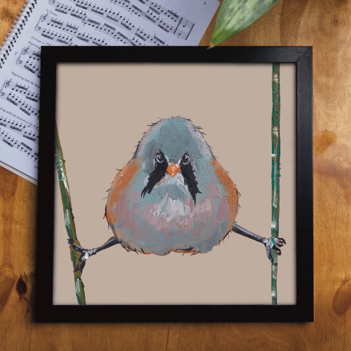 A framed small bearded tit art print featuring a small bird perched comically on reeds with a humorous expression on its face. 