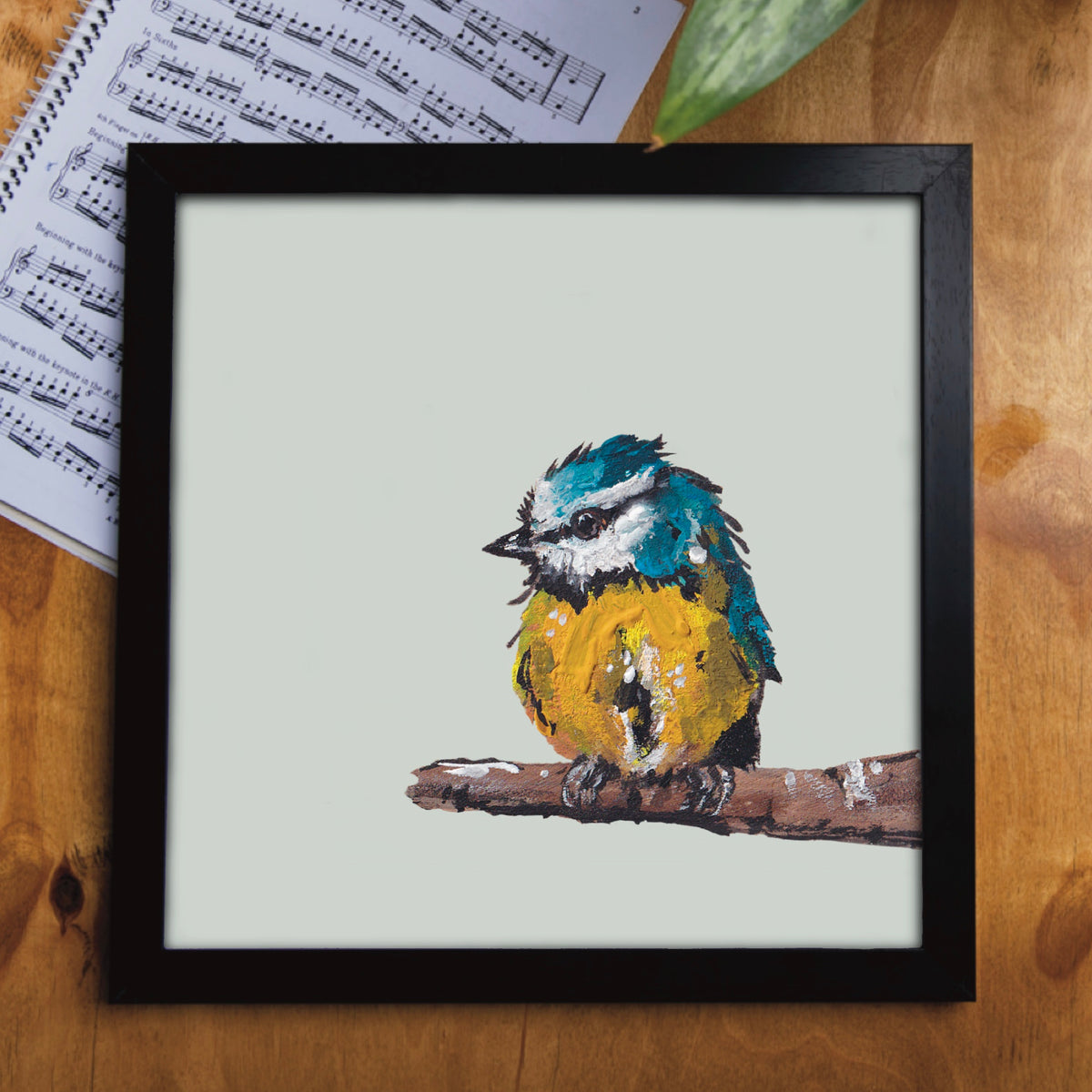 A framed front cover of a square greetings card showing an illustration of a blue tit bird. 